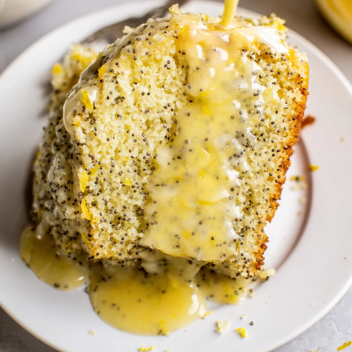 A slice of golden Lemon Poppy Seed Cake, with visible poppy seeds and tangy lemon glaze.