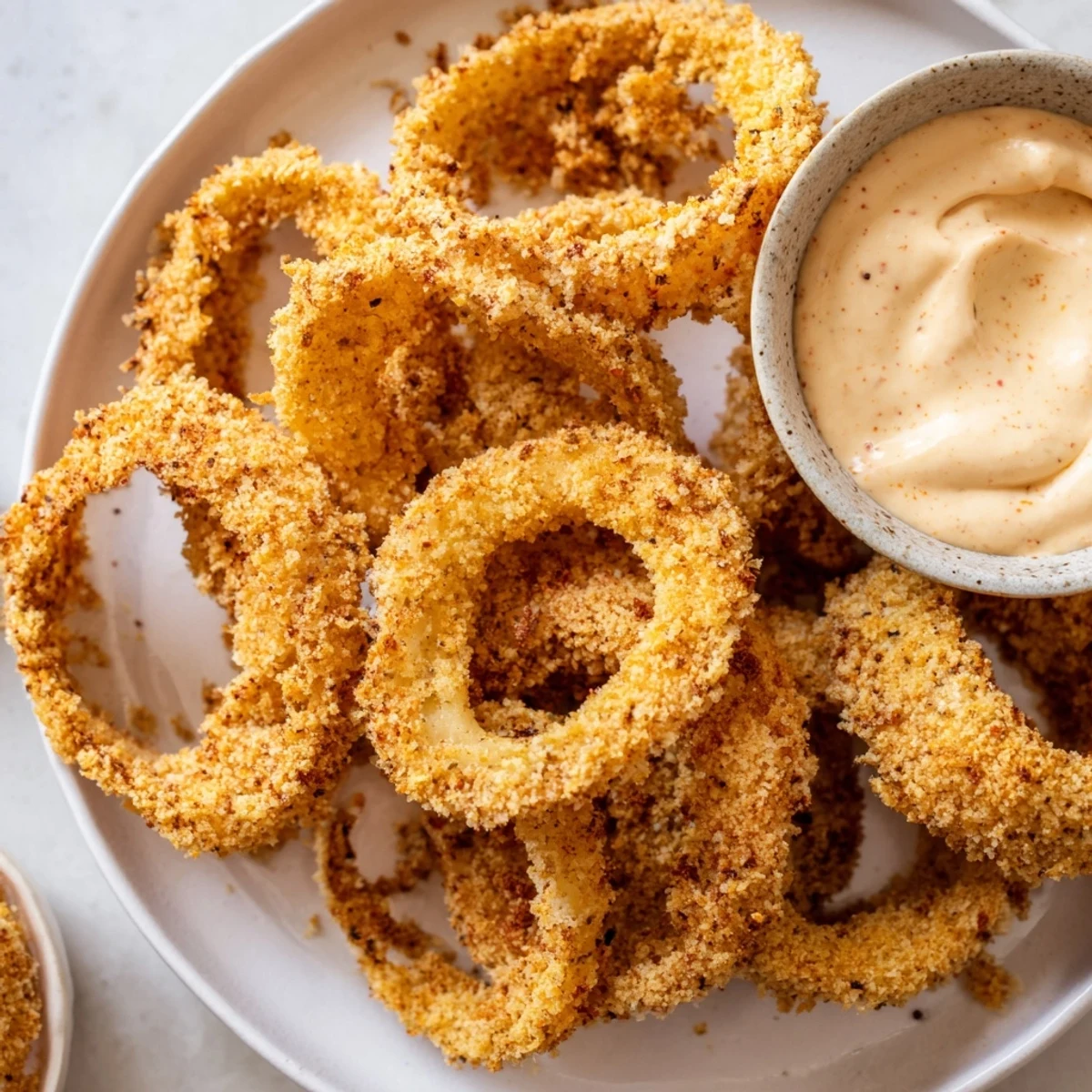 Freshly made air fryer onion rings look crispy, with a creamy sauce alongside for dipping.