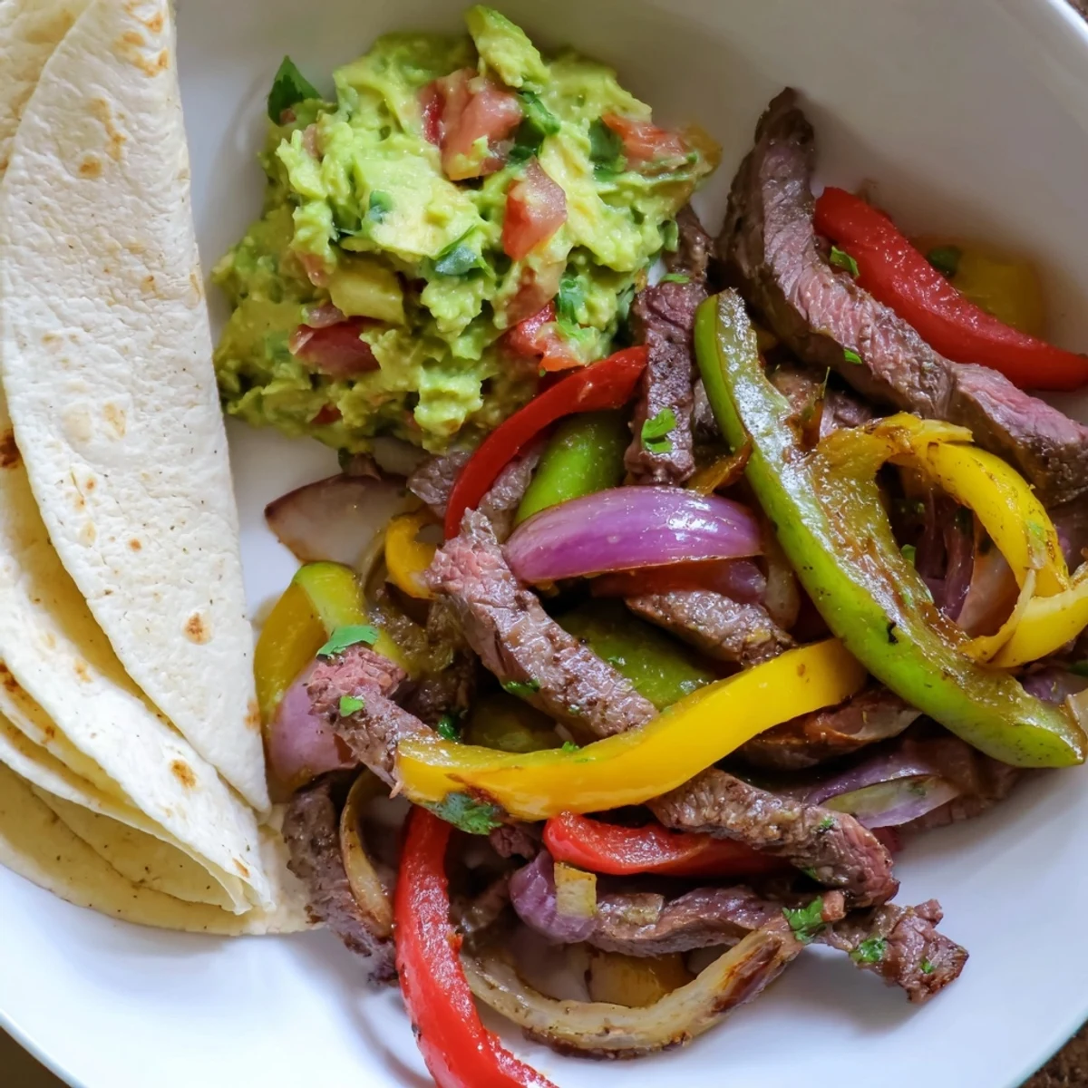 Freshly made guacamole beside sizzling beef fajitas, a flavorful Tex-Mex meal perfect for sharing.