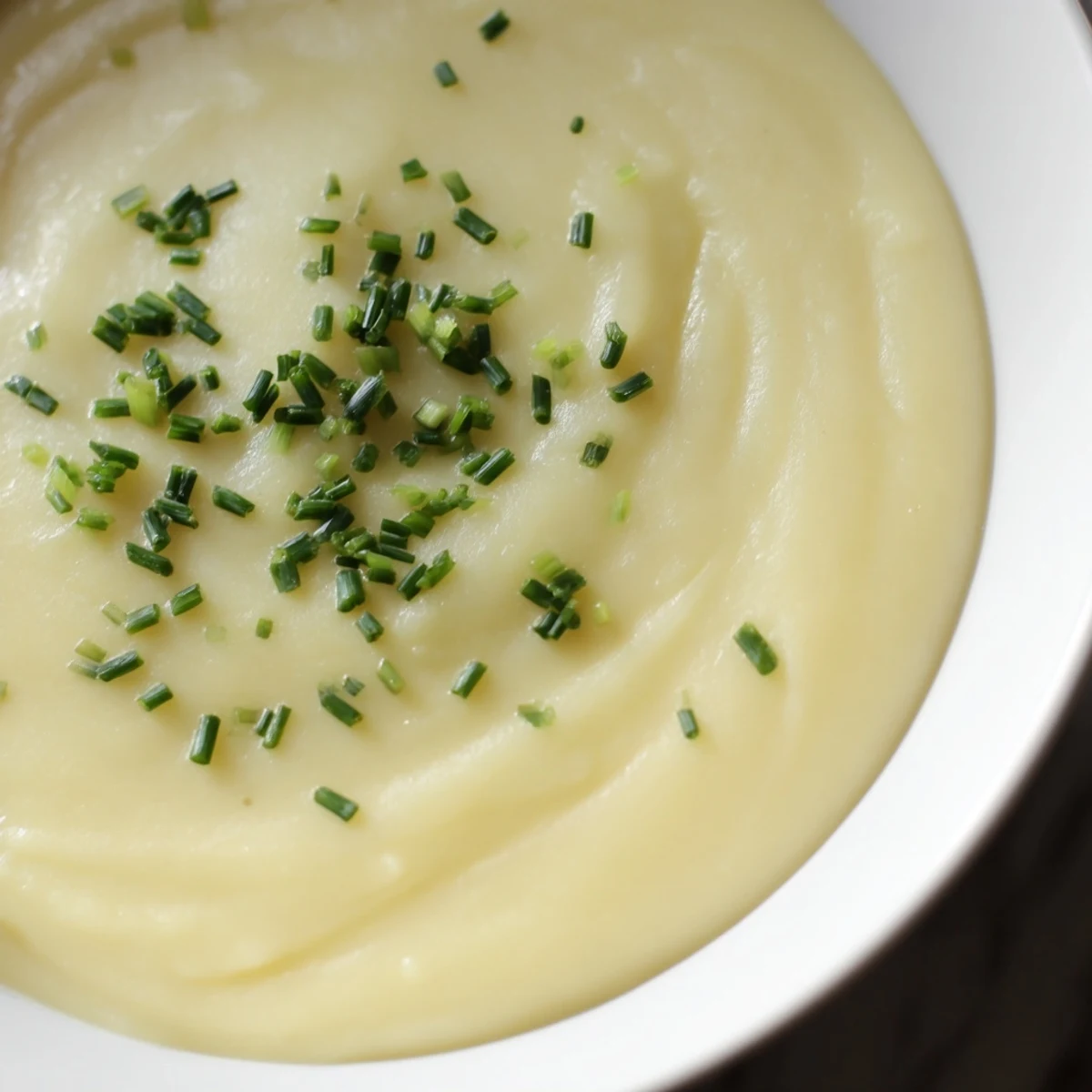 Creamy Potato Leek Soup with Chives steaming in a rustic bowl, garnished with fresh green chives and a swirl of cream.