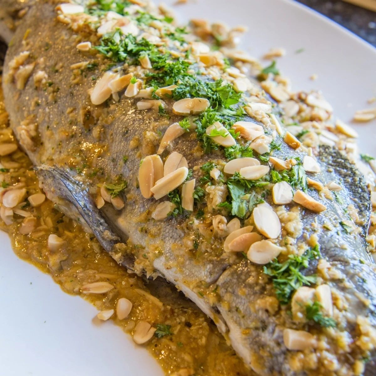 Sizzling almond butter sauce spooned over flaky, oven-roasted trout on a rustic white plate.