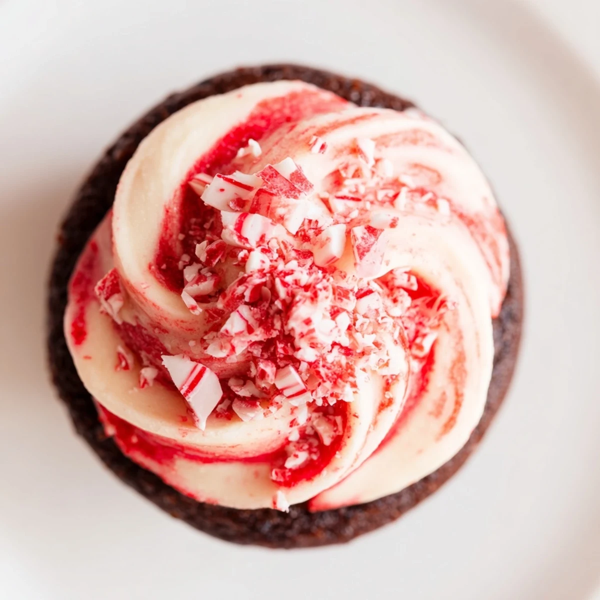 A close-up of a Chocolate Peppermint Swirl Cupcake showing moist crumb, pink frosting swirls, and peppermint pieces.