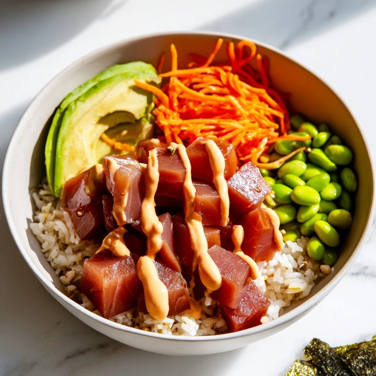 An overhead view of a fresh Spicy Tuna Poke Bowl with Sriracha Mayo, arranged with colorful edamame, pickled ginger, and vibrant carrot shreds.