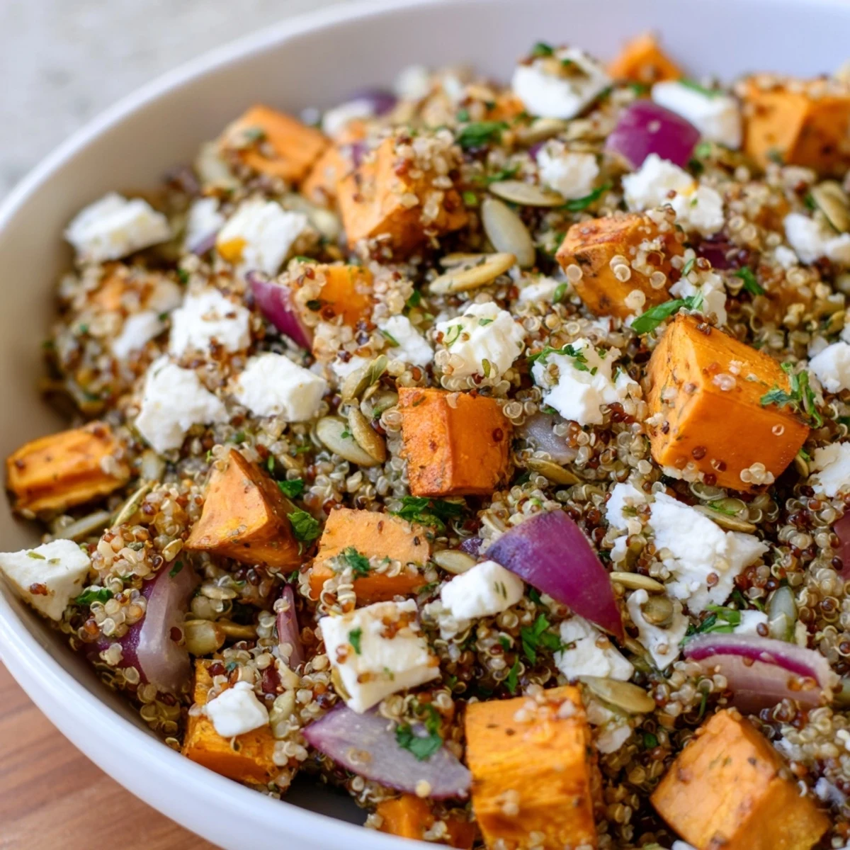 Roasted carrots and parsnips top a bowl of fluffy Warm Quinoa Salad with Roasted Root Vegetables, garnished with parsley and feta.