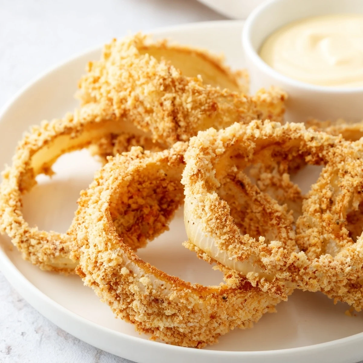 Hot Crispy Air Fryer Onion Rings with Dip stacked high on a plate with fresh lemon wedges. 