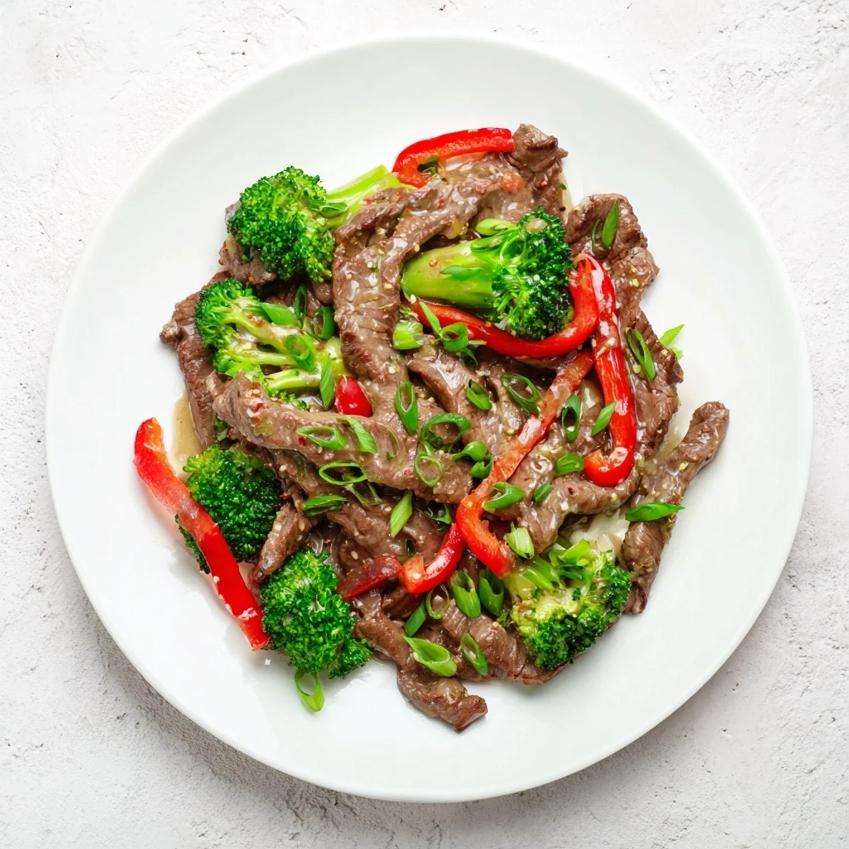 A close-up of Spicy Beef Stir Fry with Broccoli Florets glistening in a savory sauce on a plate with white rice.