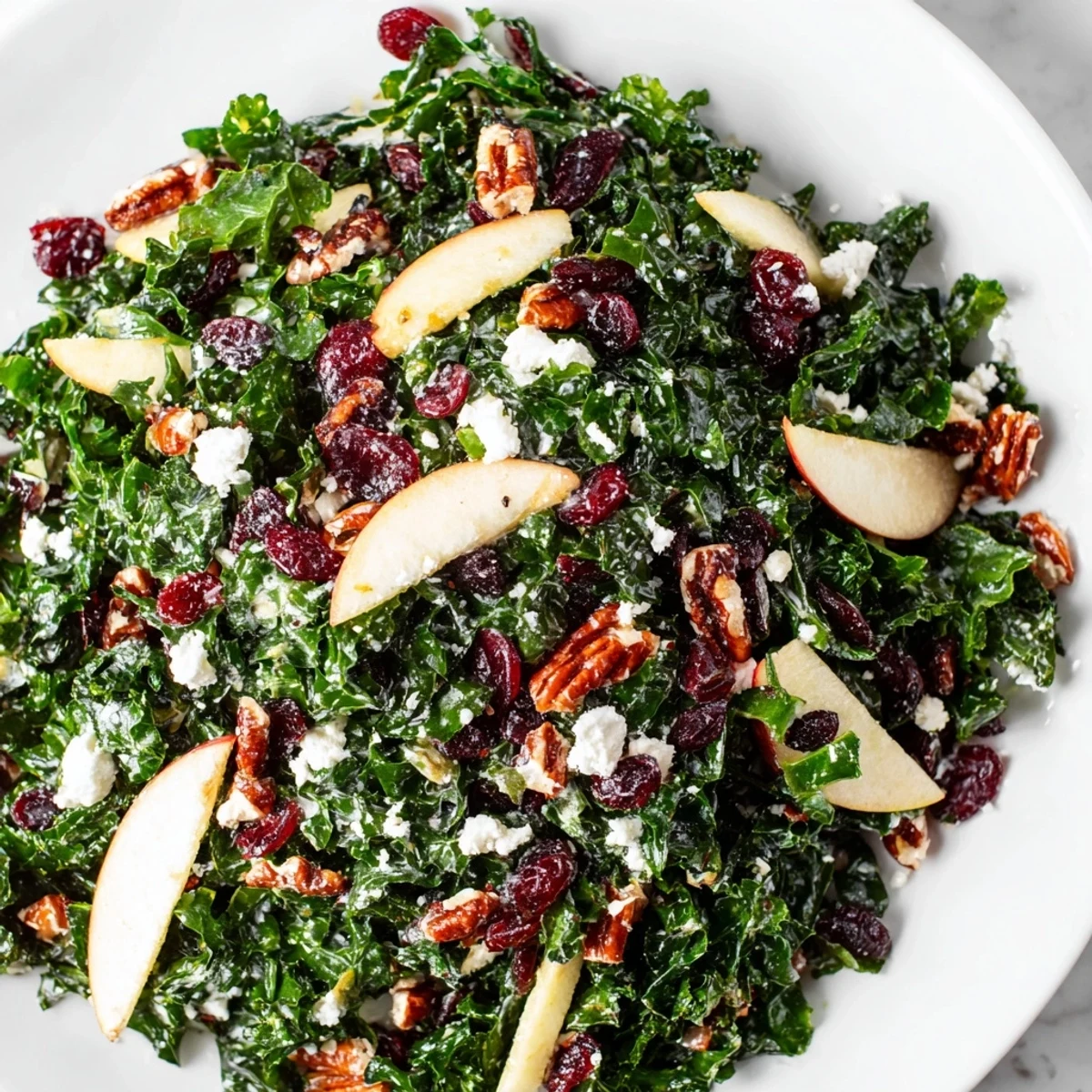 Close-up view of Winter Kale Salad with Dried Cranberries, highlighting the texture of massaged kale leaves, jewel-toned fruit, and golden toasted nuts.