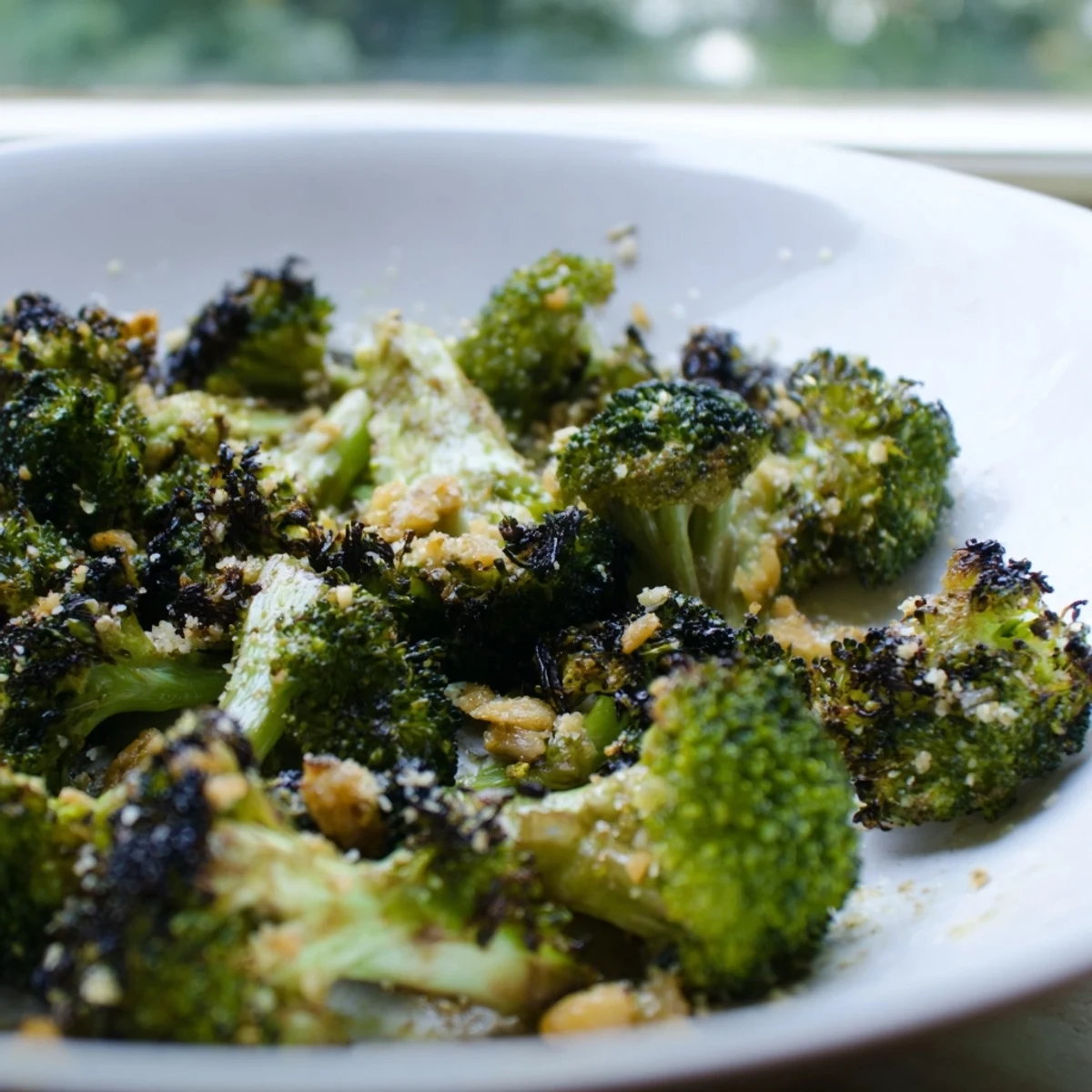 Golden, caramelized broccoli florets roasted with garlic and topped with melted Parmesan cheese on a rustic baking sheet.