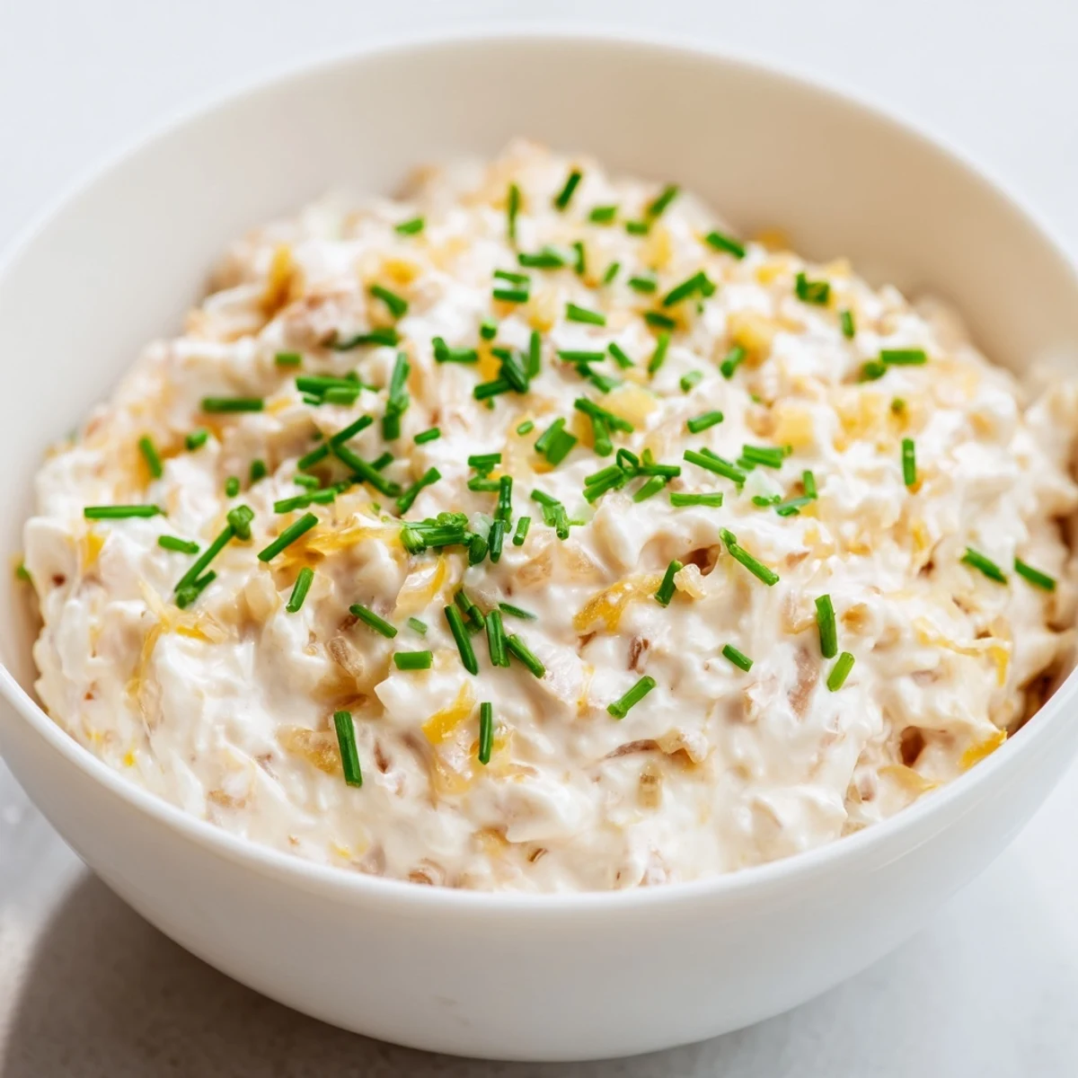 A serving bowl of Game Day Onion Dip surrounded by crispy kettle chips and fresh chives.