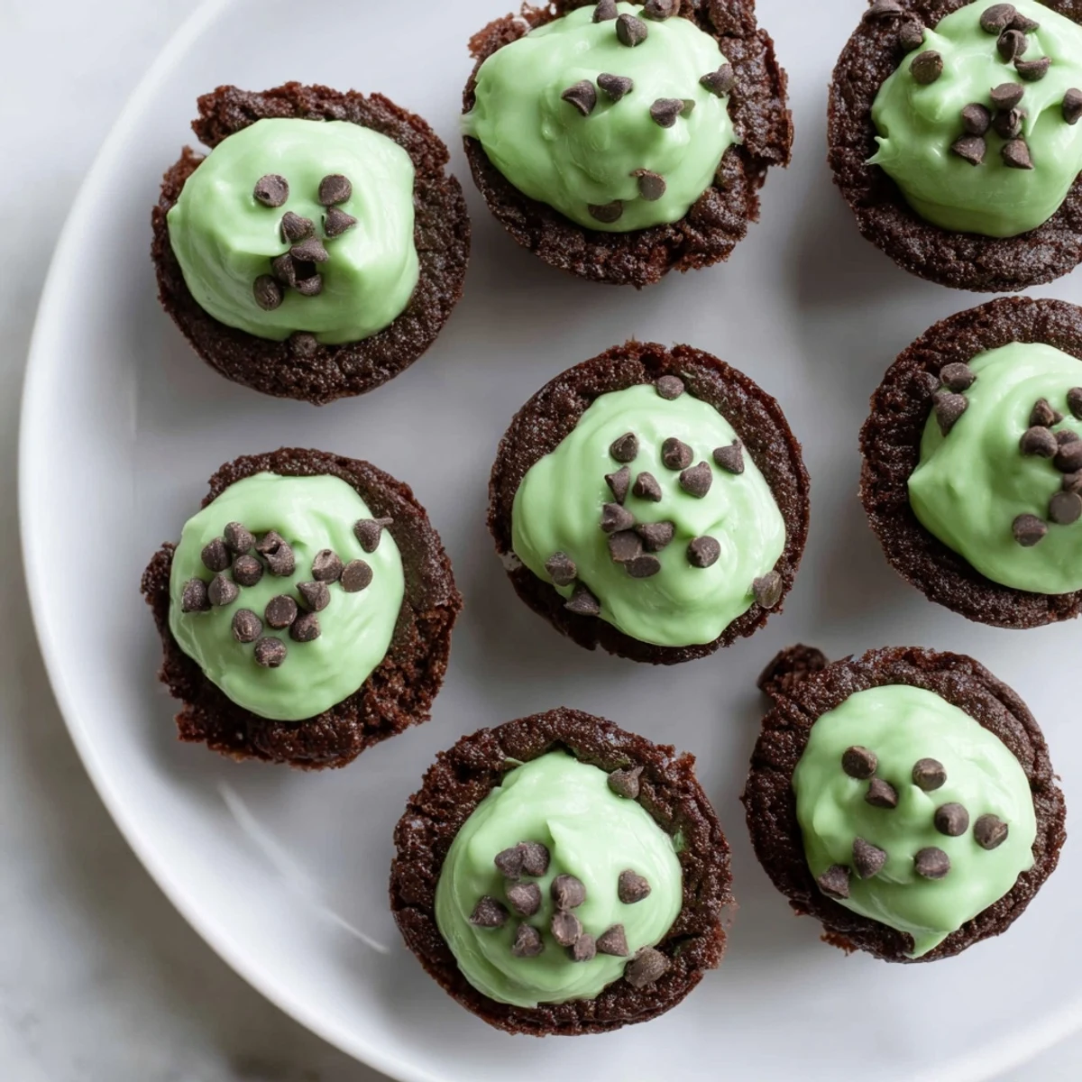 St. Patricks Day Mint Brownie Bites are plated with chocolate shavings, showing their fudgy texture and festive green frosting.