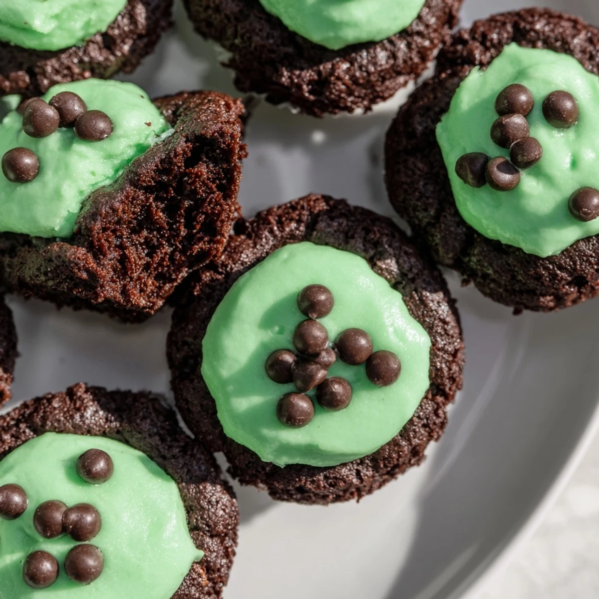 Freshly baked St. Patricks Day Mint Brownie Bites on a wooden board, topped with mint frosting and rainbow sprinkles.