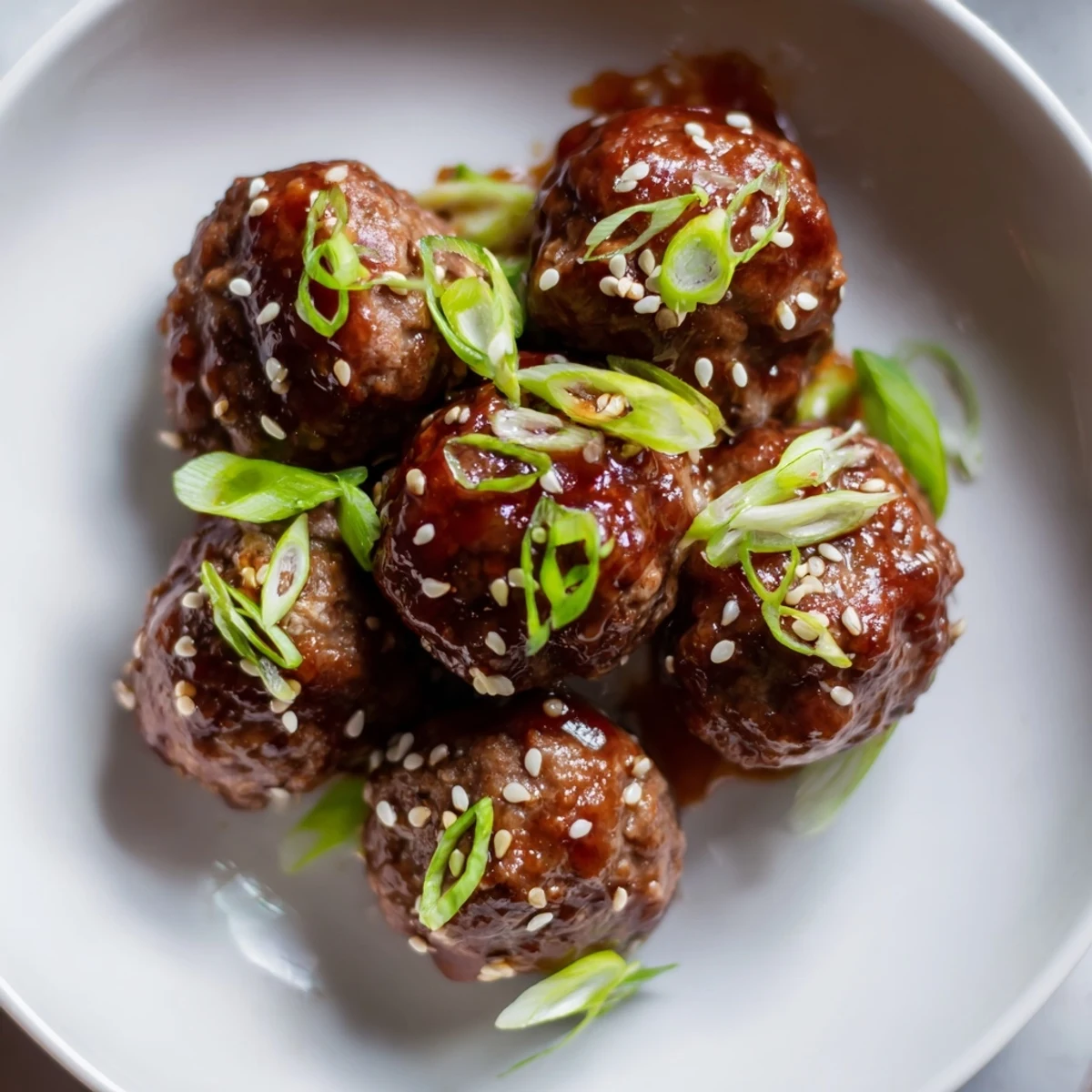Golden brown spicy Sriracha beef meatballs on a platter with sesame seeds and sliced green onions, perfect over steamed rice.