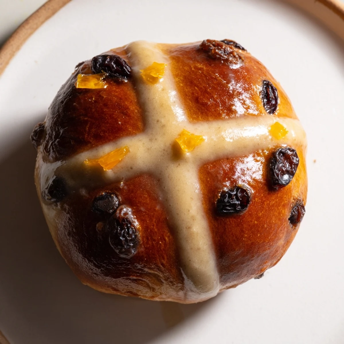 Freshly baked Hot Cross Buns with currants and spices, glistening with apricot glaze, arranged on a rustic wooden board for a cozy Easter morning breakfast.