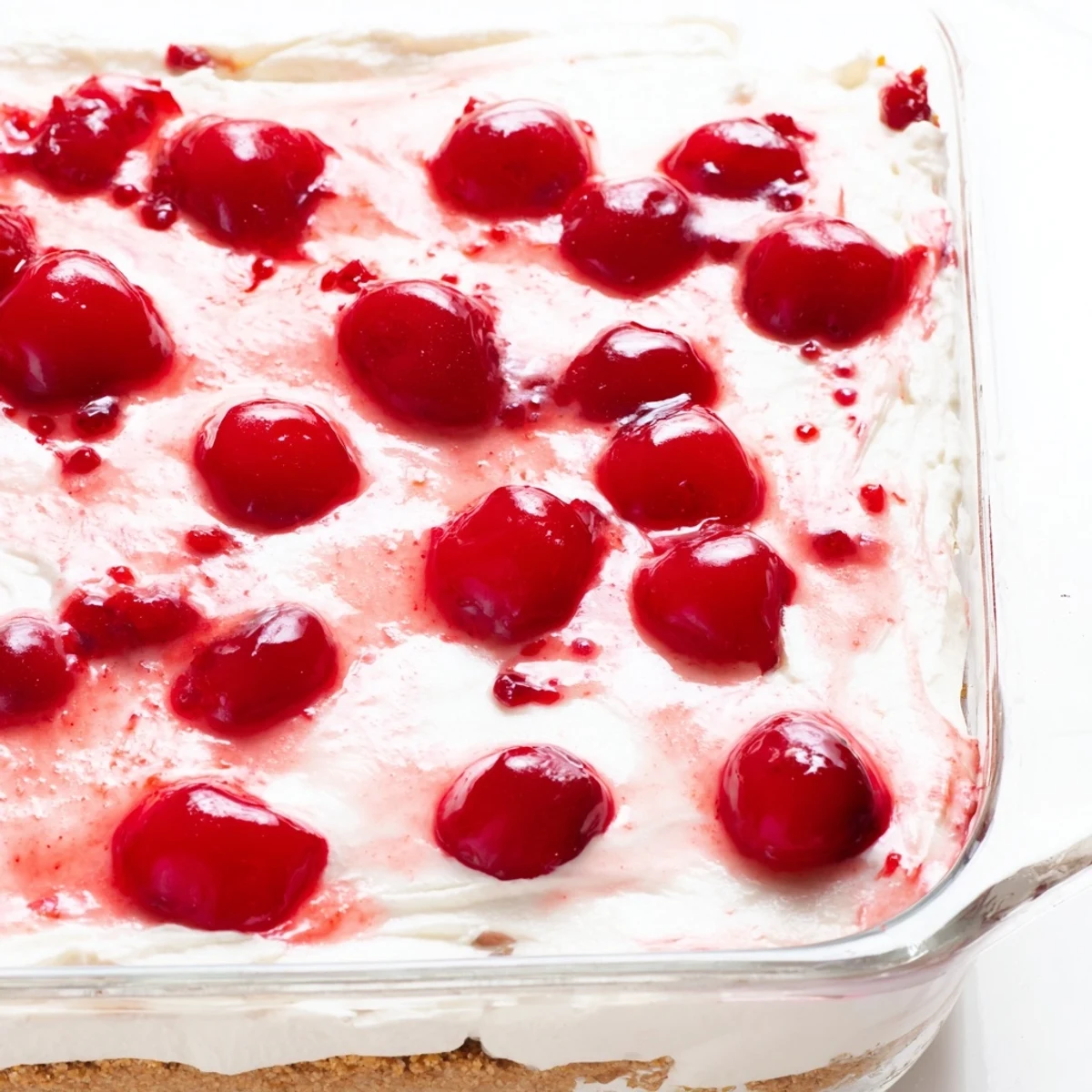 Slice of Classic Cherry Delight on a white plate, highlighting the smooth cream cheese layer, graham cracker base, and sweet cherry garnish.