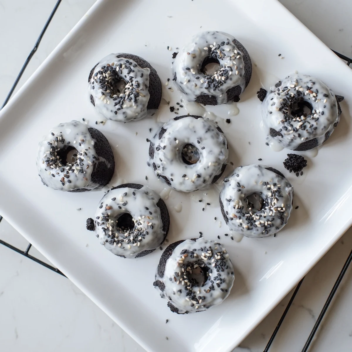 Glazed Black Sesame Mochi Donuts arranged on a white plate, with a sweet glaze and sesame seed toppings.