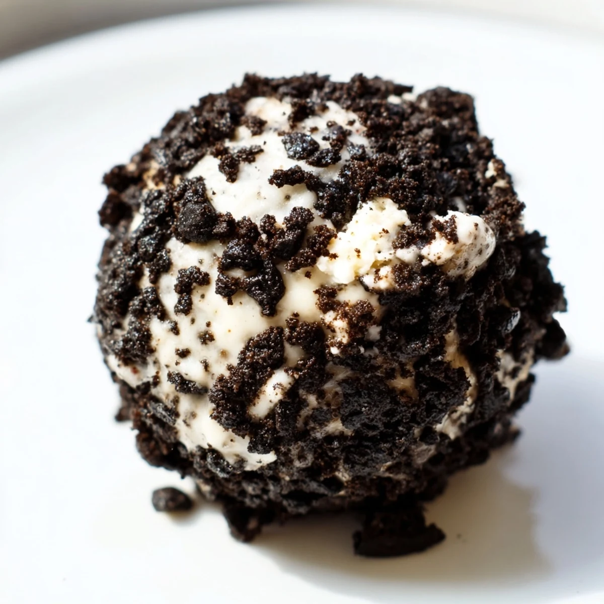 Close-up of freshly rolled Cream Cheese Oreo Protein Balls coated in dark cookie crumbs on a marble slab.