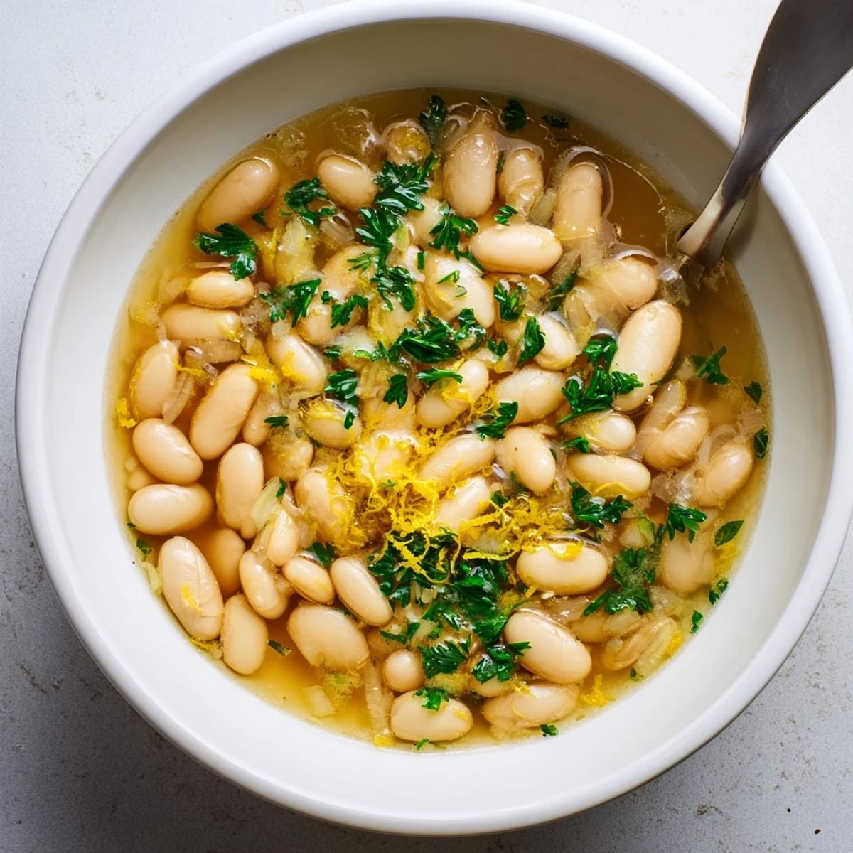 Creamy Miso Butter Brothy Beans in a white bowl, garnished with fresh parsley and lemon zest, served beside crusty bread.  