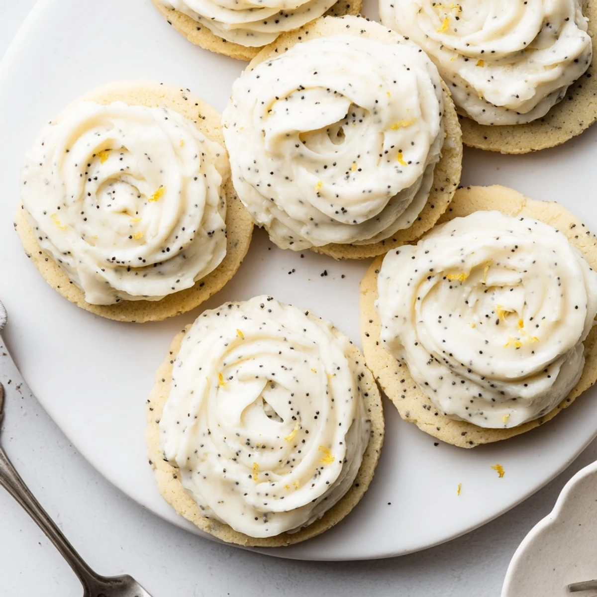 Stack of lemon poppy seed cookies topped with swirls of creamy cheesecake frosting