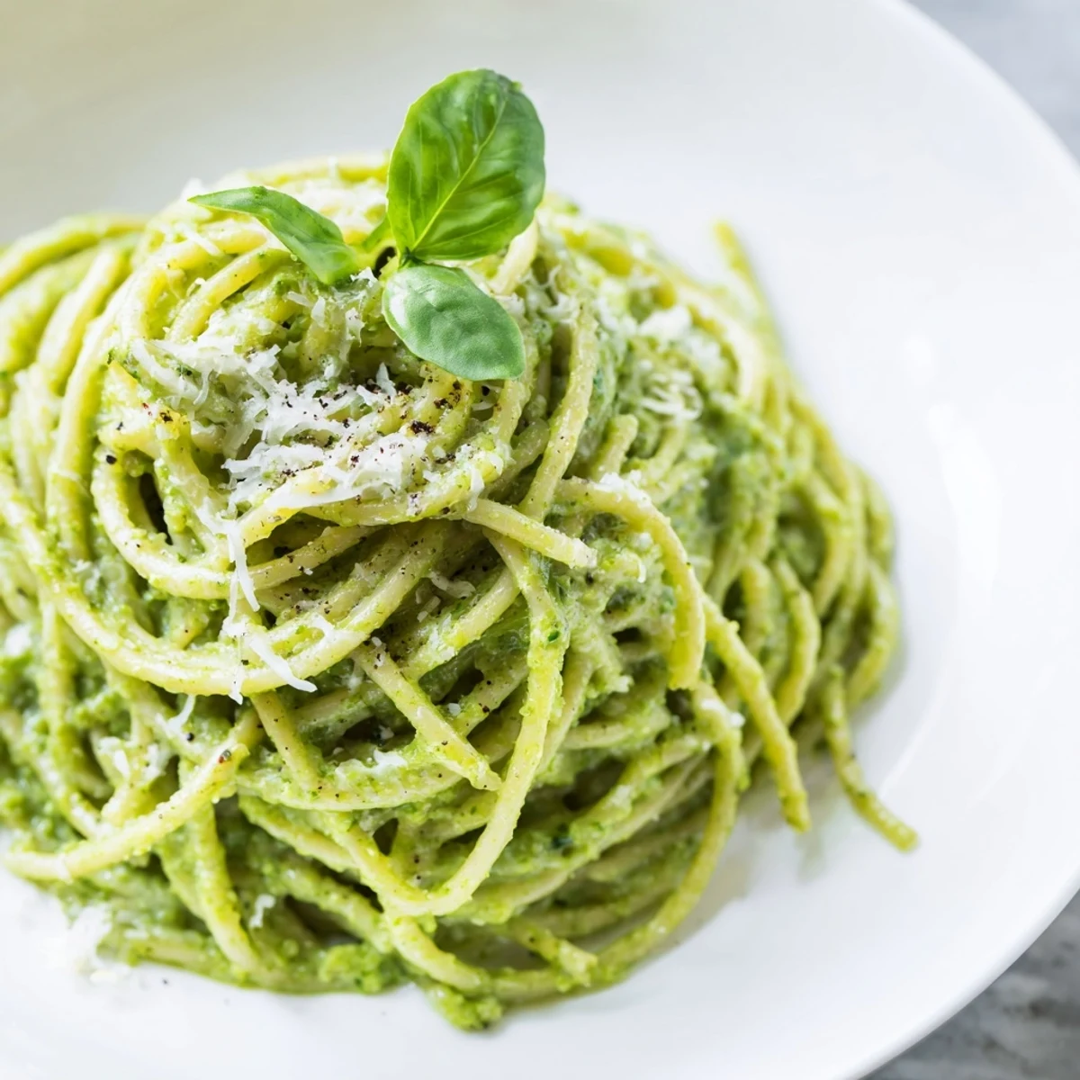 Bright green avocado pesto pasta dish tossed with al dente spaghetti noodles and fresh basil garnish
