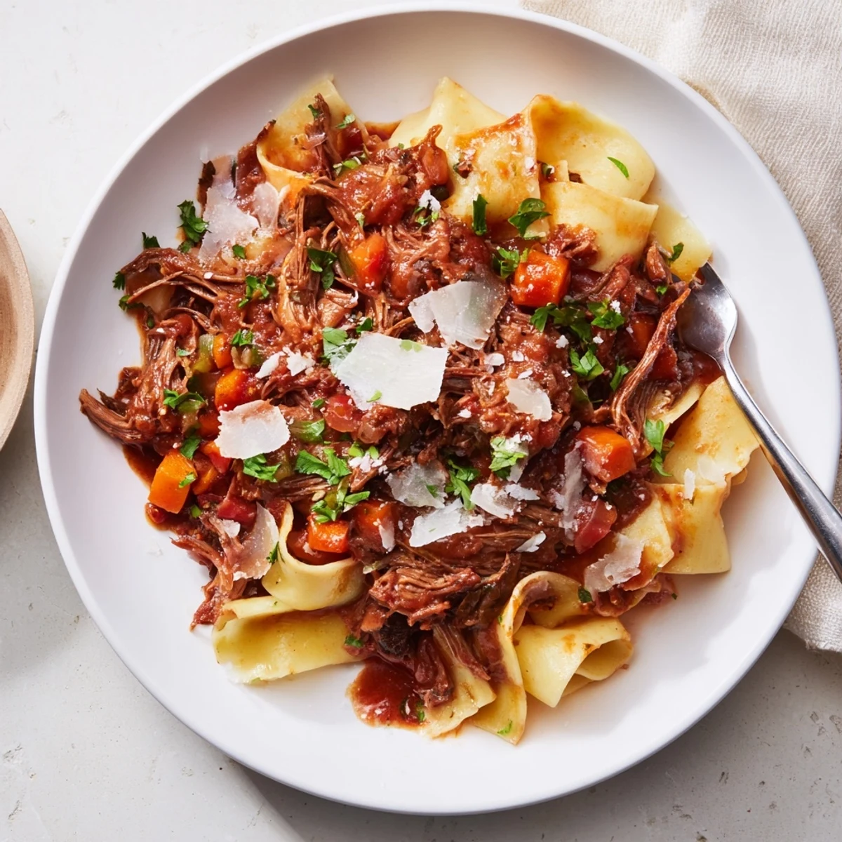 Golden brown lamb ragu sauce coats wide pappardelle pasta noodles generously with freshly grated Parmesan cheese