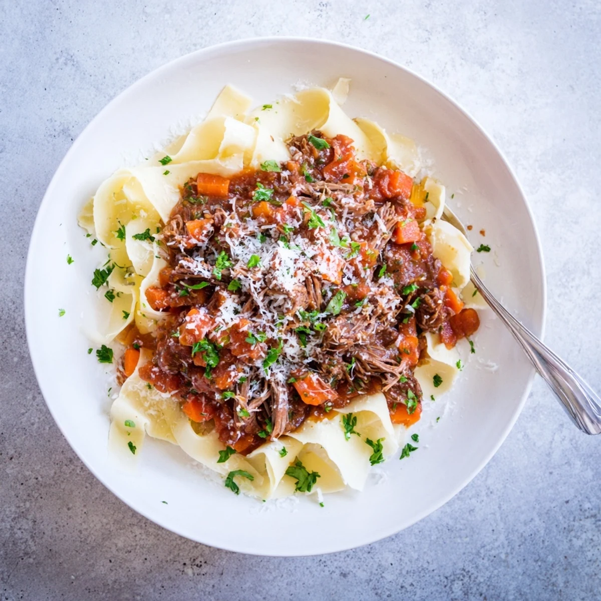 Slow braised lamb ragu with tender meat chunks served over silky pappardelle pasta in a rustic shallow bowl