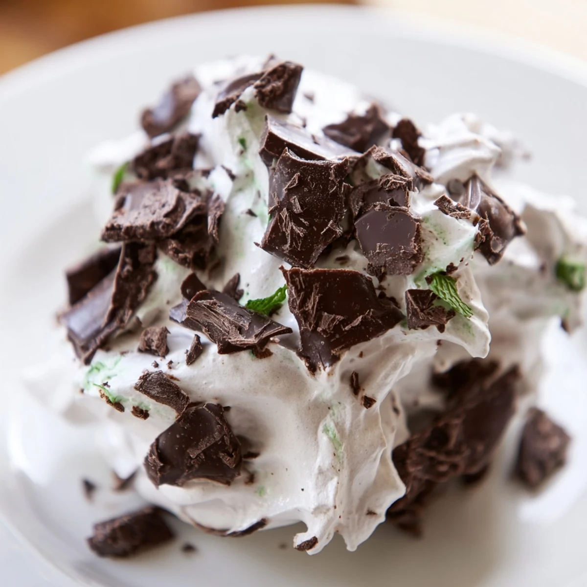 Fluffy dark chocolate and mint chip clouds meringue cookies piled on a white serving plate