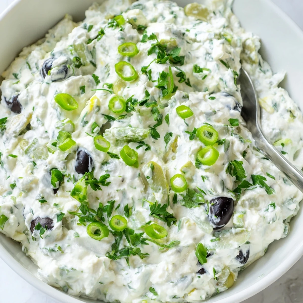 Cream cheese olive dip served in a white bowl with assorted crackers and fresh vegetables