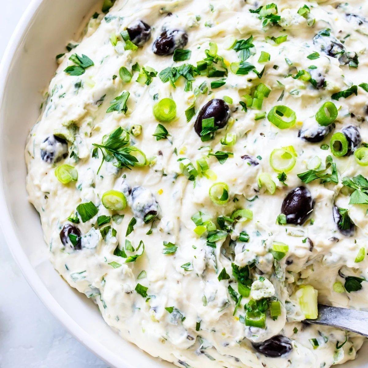 Tangy cream cheese olive spread displayed on rustic wooden board alongside colorful vegetable crudités