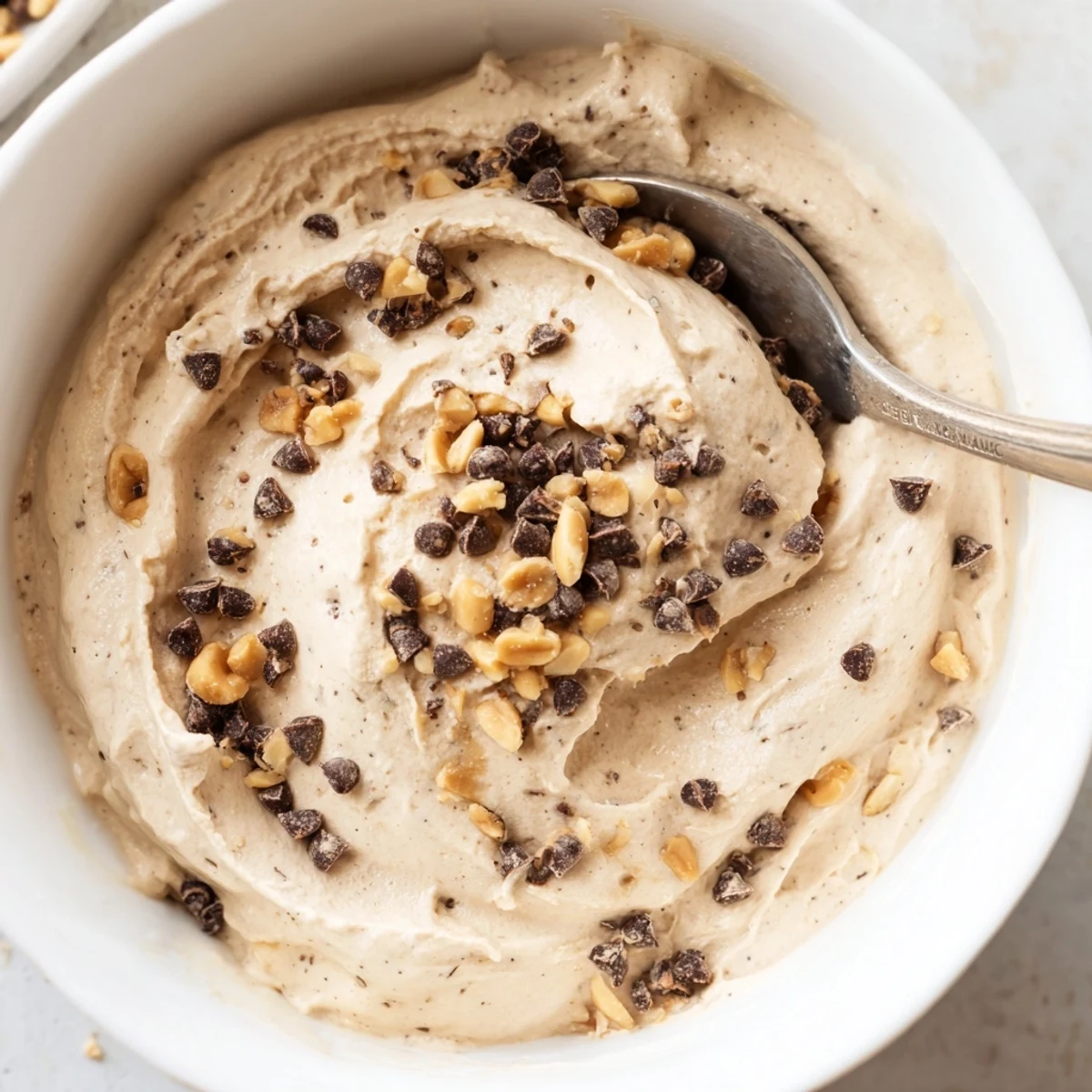 Creamy peanut butter and Cool Whip mousse topped with chopped roasted peanuts and mini chocolate chips in a clear glass bowl