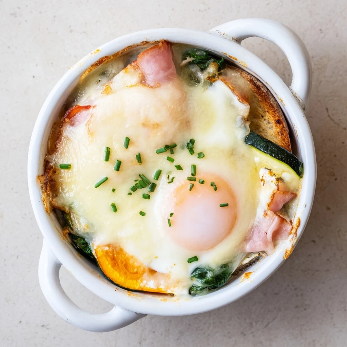 Golden baked eggs Napoleon with creamy cheese sauce in individual white ramekins