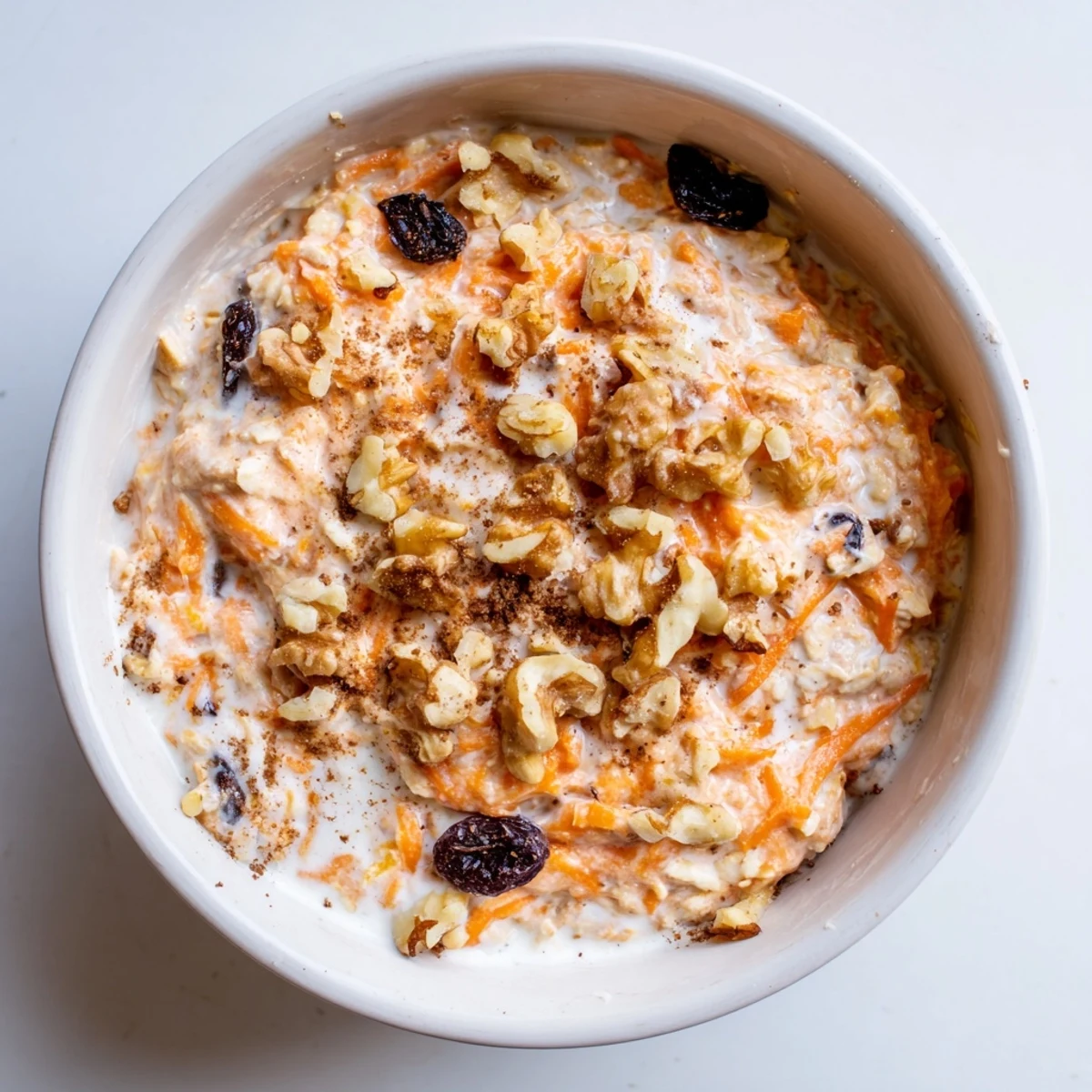 Spoonful of spiced carrot cake overnight oats showing grated carrots, raisins, and a thick creamy texture