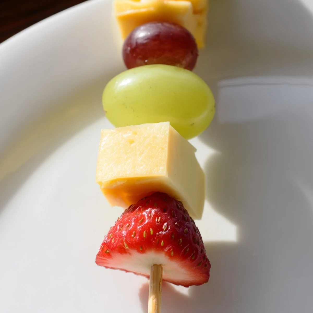 Colorful fruit and cheese kabobs arranged on a platter with grapes, strawberries, pineapple, and cheddar cubes