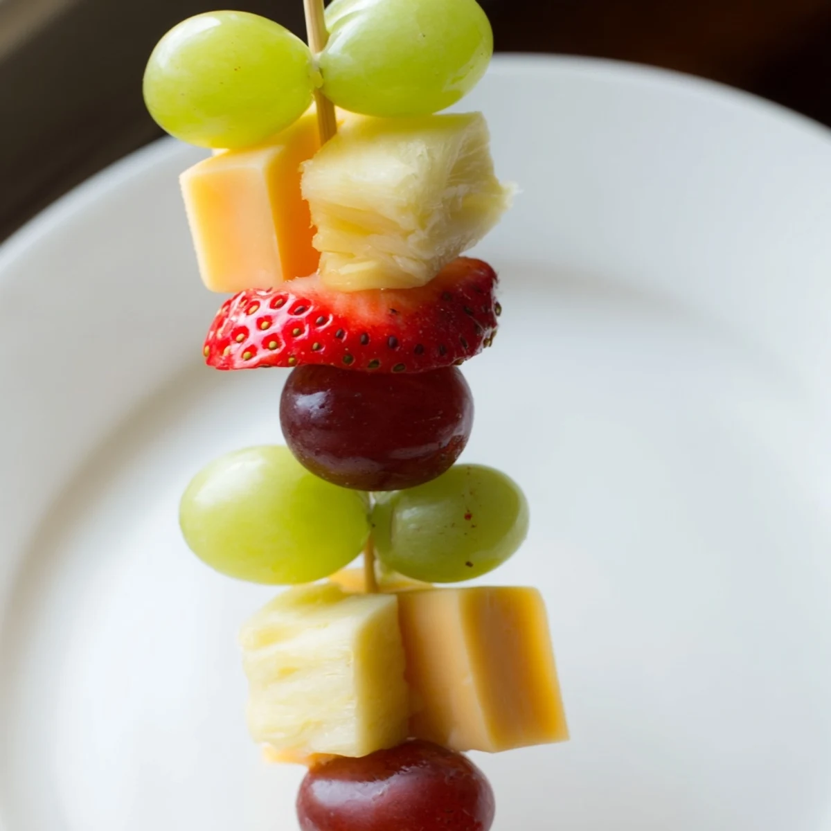 Fresh fruit and cheese kabobs featuring alternating cubes of cheddar, mozzarella, red grapes, and sweet pineapple chunks