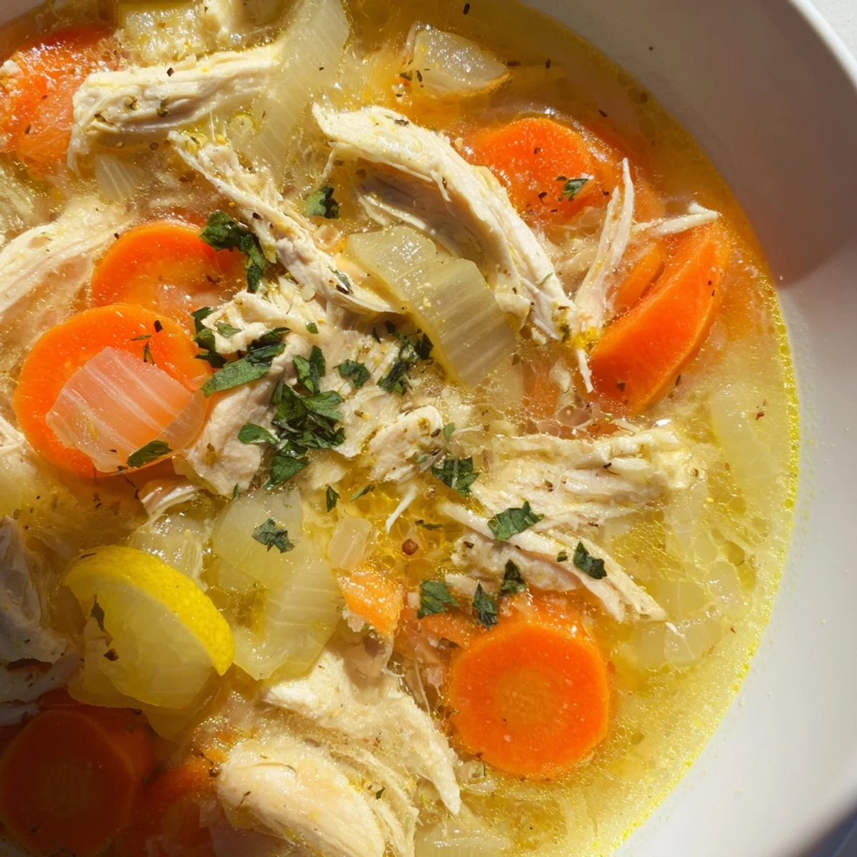 Steaming bowl of Crockpot Lemon Chicken Soup garnished with fresh parsley and lemon slices