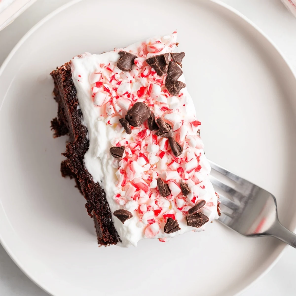 Festive Peppermint Poke Cake topped with minty pudding, whipped cream, crushed candies.