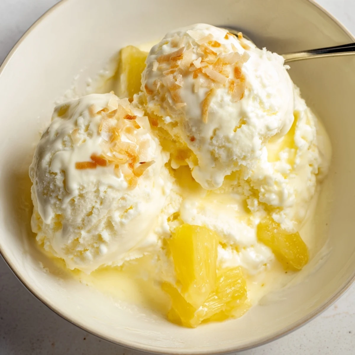 Creamy Pineapple Ice Cream crowned with toasted coconut, spoon melting glossy swirls