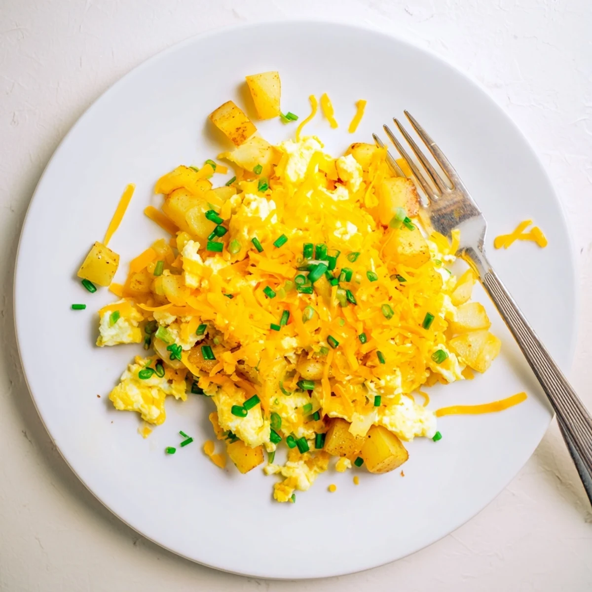 Golden cheesy potato egg scramble with melted cheddar and soft fluffy curds on a white plate
