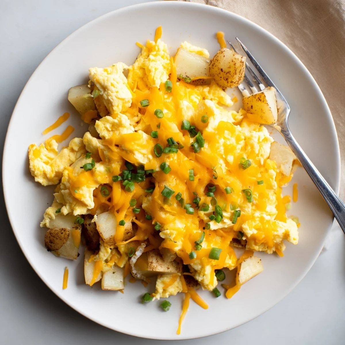 Comforting cheesy potato egg scramble garnished with fresh chives ready for a warm brunch meal