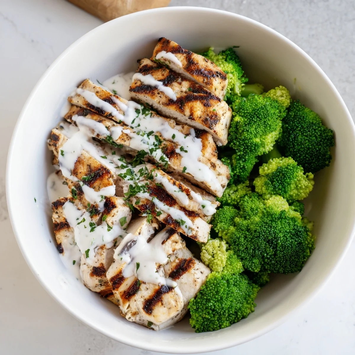 Healthy grilled chicken broccoli bowls with creamy garlic sauce drizzled over tender sliced chicken and crisp steamed broccoli florets
