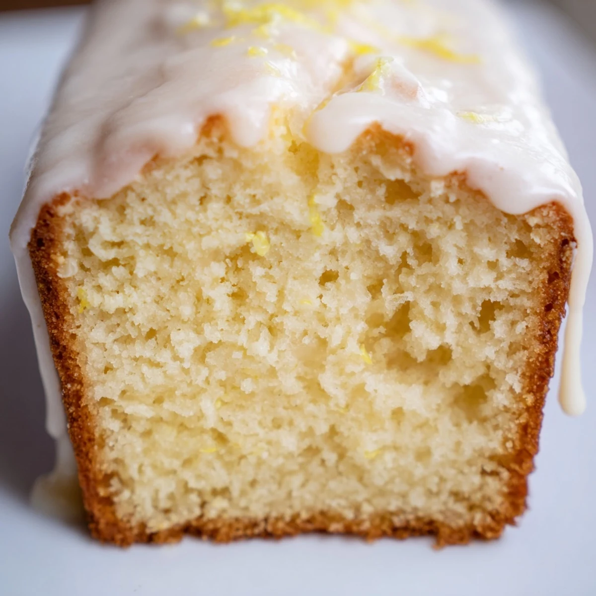 Golden Greek yogurt lemon loaf drizzled with white glaze on a white serving plate