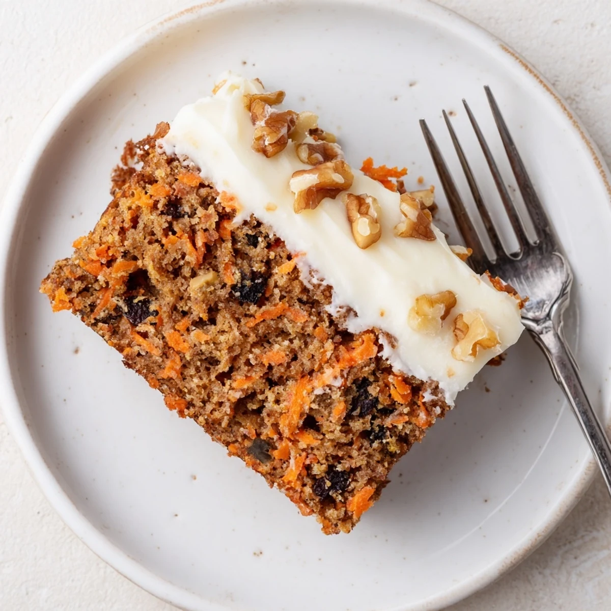 Golden slice of flourless oatmeal carrot cake topped with chopped walnuts on a white plate