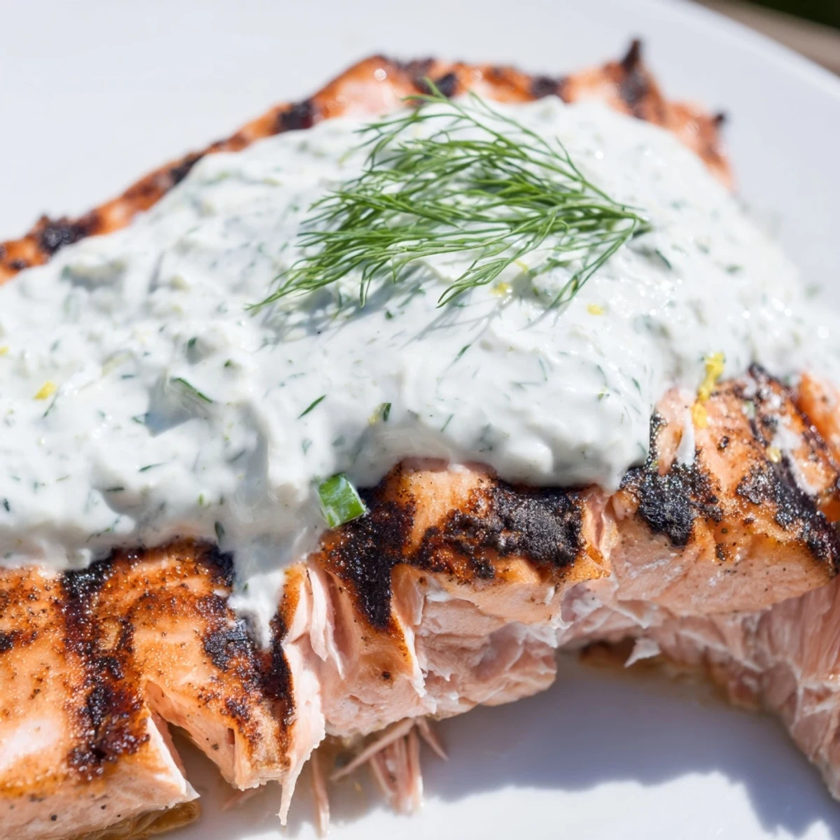 Lemon herb grilled salmon resting on a white plate with creamy yogurt dipping sauce