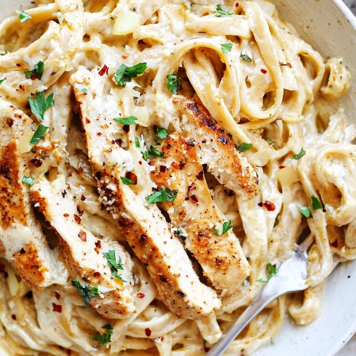 Steaming bowl of creamy garlic parmesan chicken pasta topped with fresh parsley and extra grated Parmesan