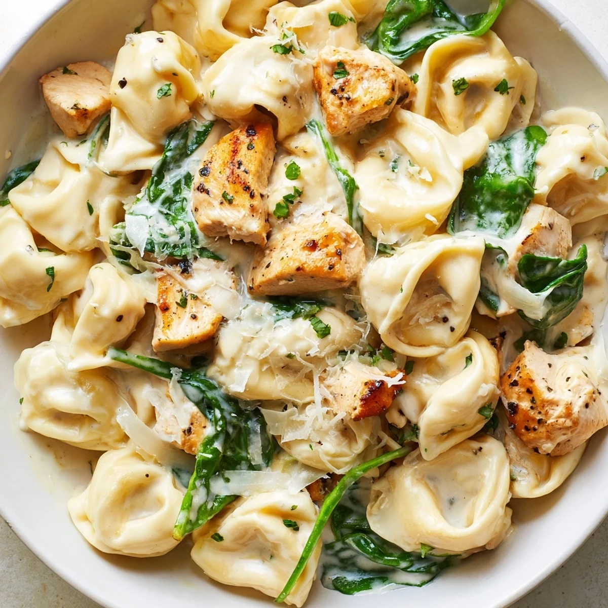 Creamy garlic chicken tortellini with spinach served in a white bowl with Parmesan