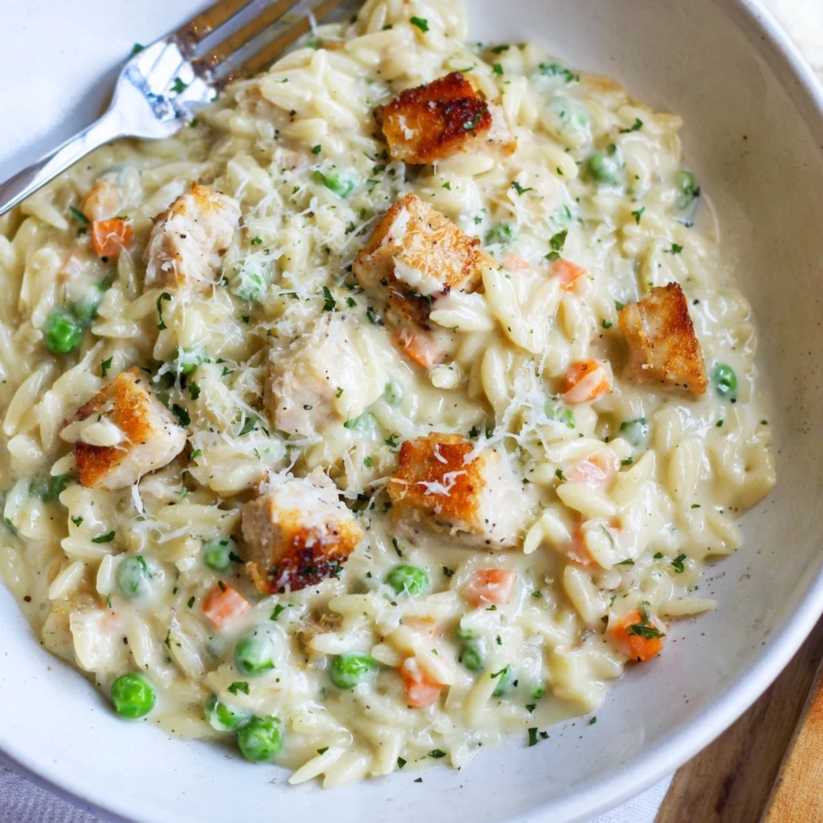 Creamy Chicken Pot Pie Orzo with colorful diced carrots, peas, and savory chicken on a wooden spoon.