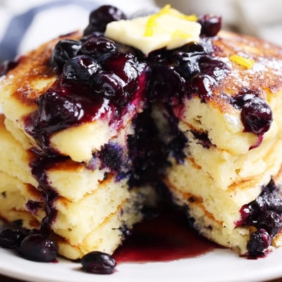 Fluffy Lemon Ricotta Pancakes topped with sweet blueberry syrup, served hot on a rustic plate with fresh fruit nearby.