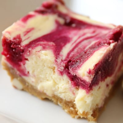Sliced Raspberry White Chocolate Cheesecake Bars arranged on a rustic wooden board, perfect for a sweet party dessert platter.