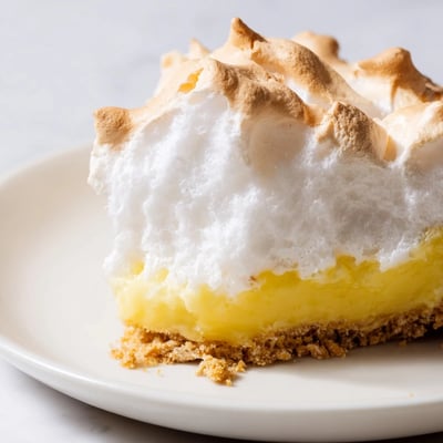 Freshly sliced wedges of Lemon Meringue Pie with Graham Cracker Crust sit on a white plate, revealing the creamy texture and bright citrus color.