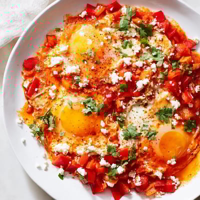 Bright red shakshuka sauce simmers in a skillet with poached eggs and fresh cilantro garnish.