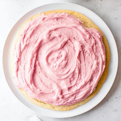 Close-up of a Giant Chilled Crumbl Sugar Cookie showing its soft, thick center and a generous dollop of vibrant pink vanilla frosting.